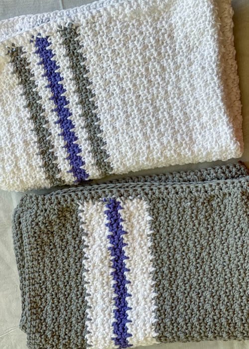 Two folded crochet kitchen towels in white, gray, and blue colors