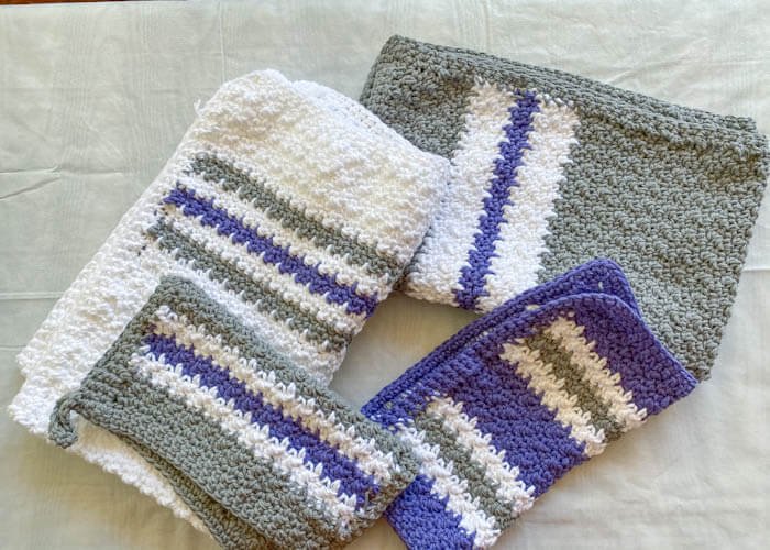 Two white and gray towels and two blue and grey kitchen towels and potholders displayed on white surface