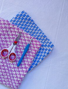 two potholders laying below scissors and a crochet needle