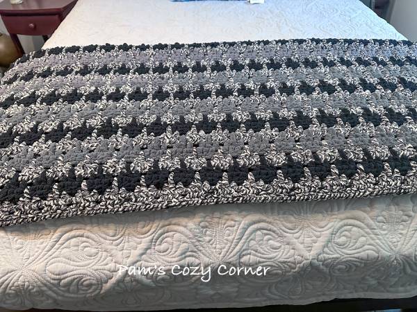 Easy crochet chunky blanket displayed on a bed in teal, green, and vanilla colors